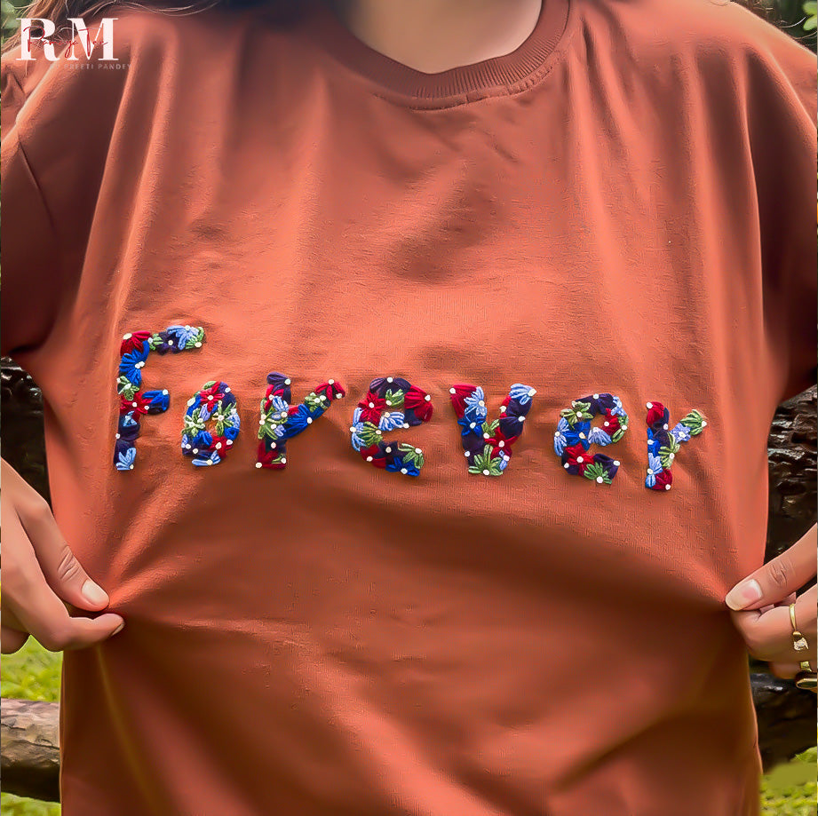 Brown t-shirt with colorful 'FOREVER' text held by a person outdoors.