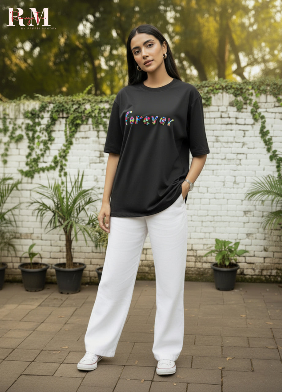 Person wearing a black t-shirt with colorful text and white pants standing outdoors.