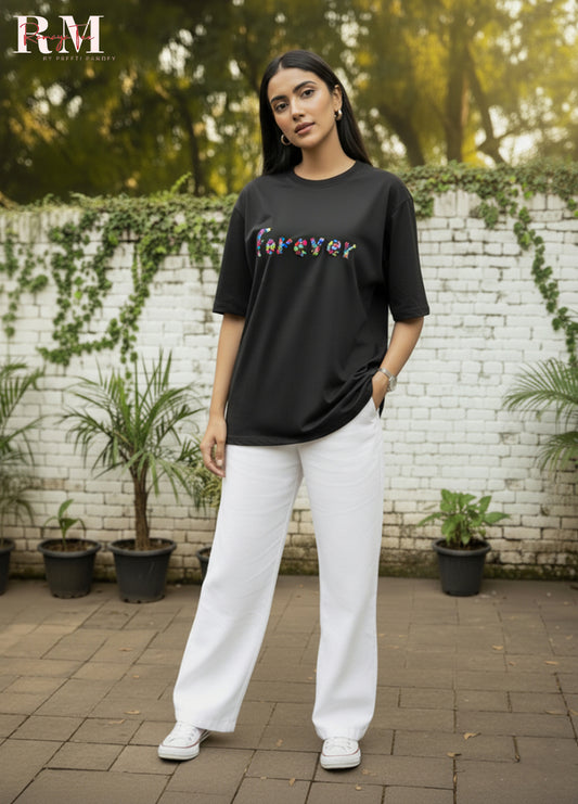Person wearing a black t-shirt with colorful text and white pants standing outdoors.