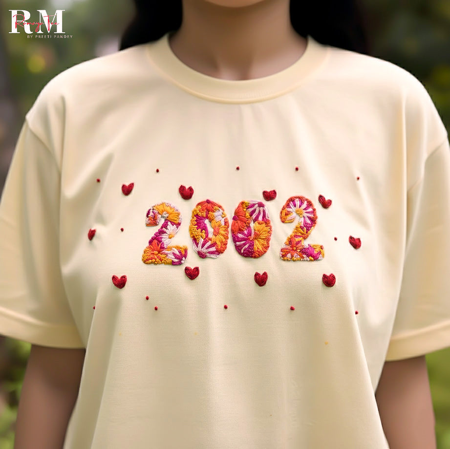 Beige t-shirt with floral '2002' design and red hearts worn by a person outdoors.